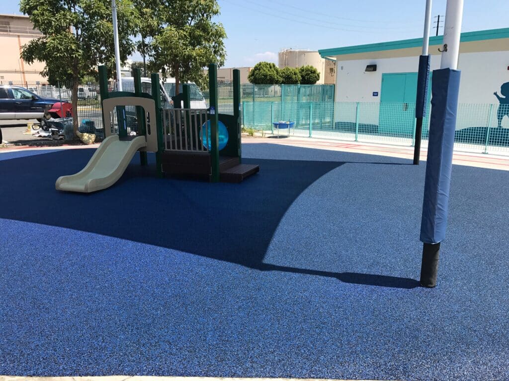 Blue poured-in-place rubber under a play structure beside a building