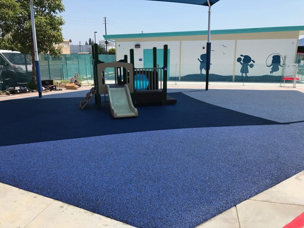 Blue poured-in-place rubber playground with a play structure at a school