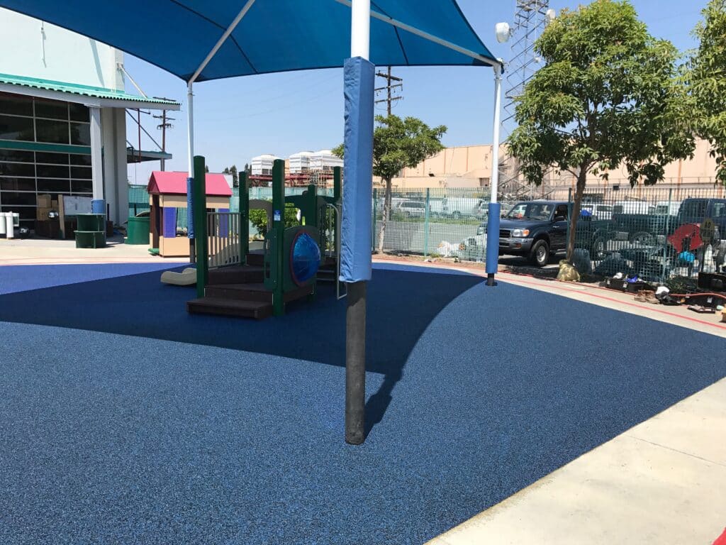 Blue poured-in-place rubber under a shade structure at a playground