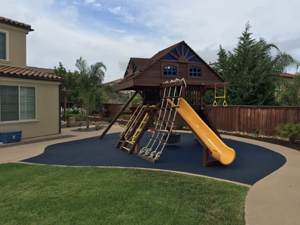 Wooden play set with a slide on rubber surfacing in a backyard