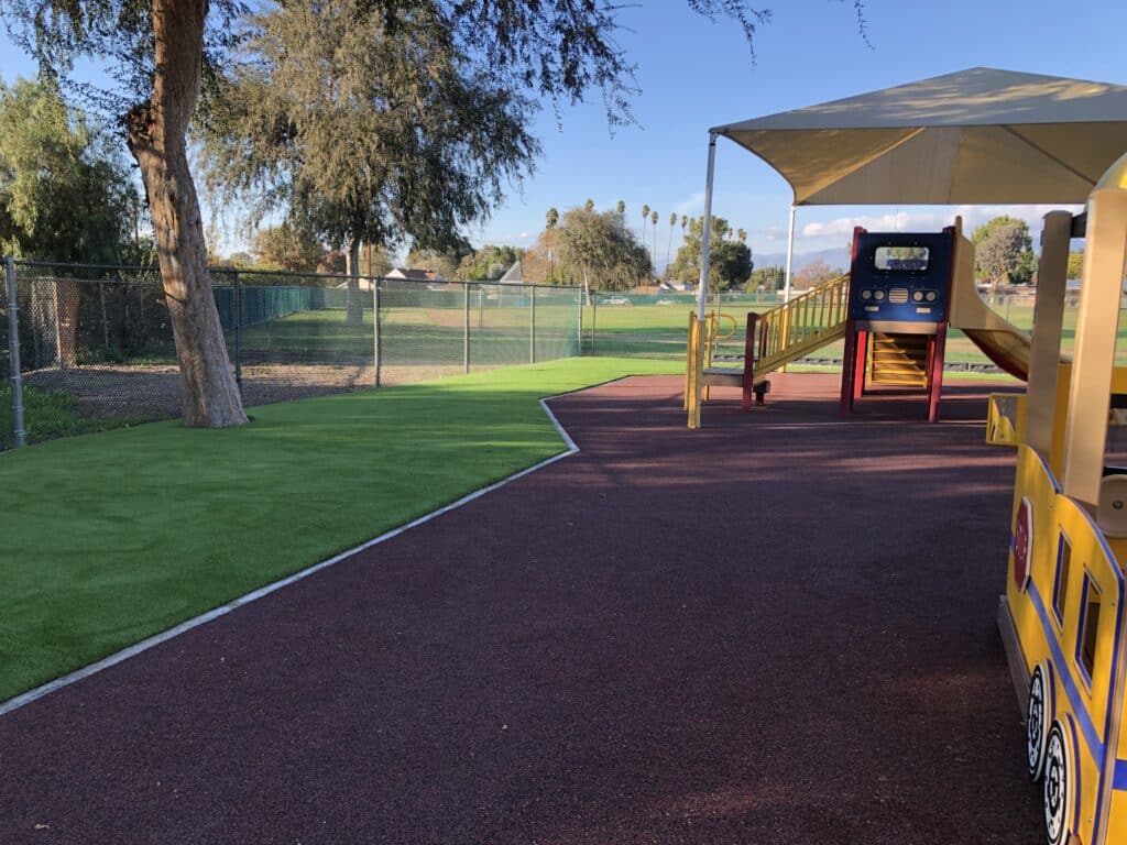 Red rubber surfacing beside a lawn and play equipment at a park
