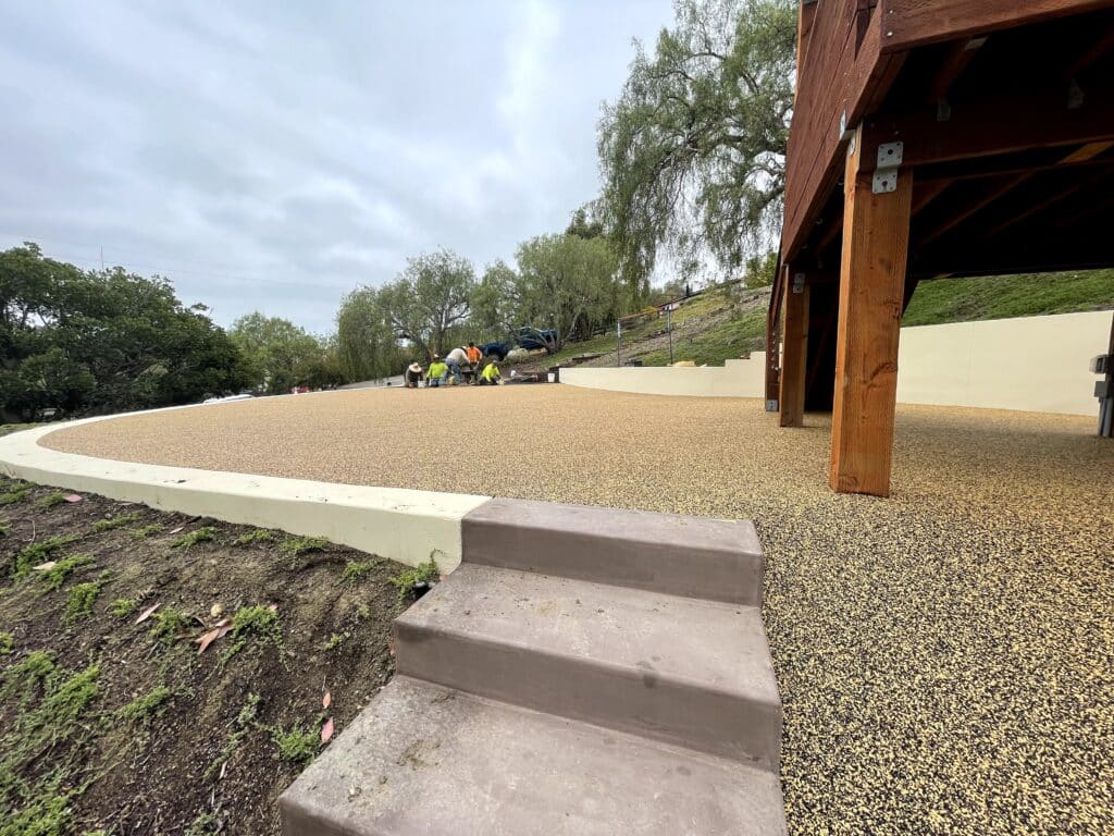 Tan porous rubber path at the base of concrete steps beside a play structure