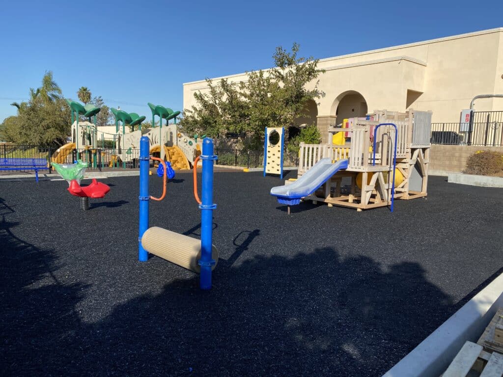 Dark poured-in-place rubber surface under a play structure next to a building
