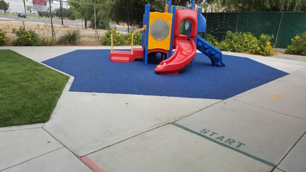 Commercial playground with blue poured-in-place rubber and a red and blue play structure