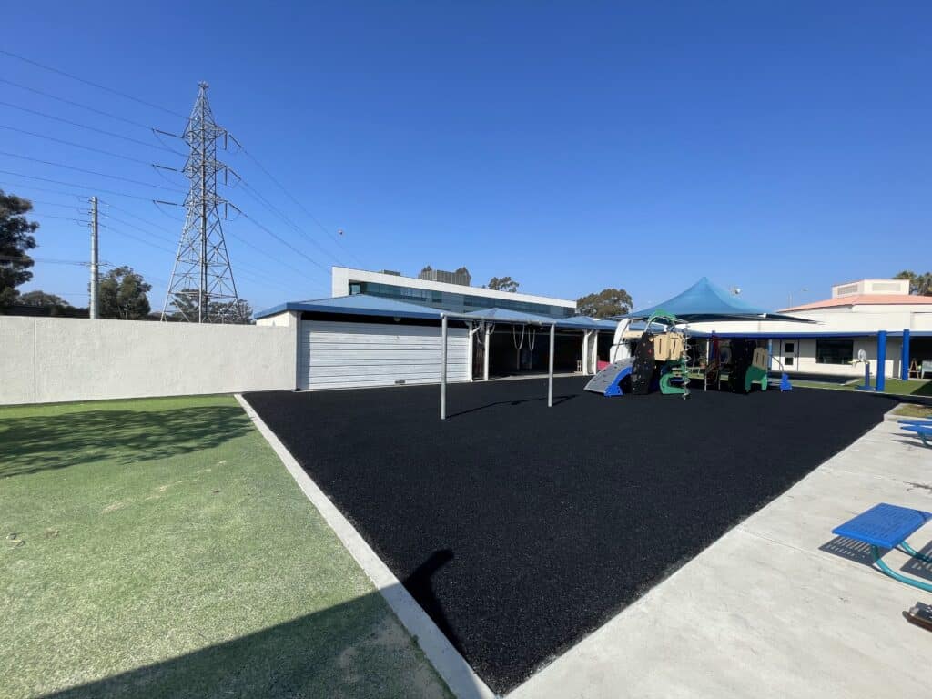 Black poured-in-place rubber fitness area next to synthetic turf at a corporate campus