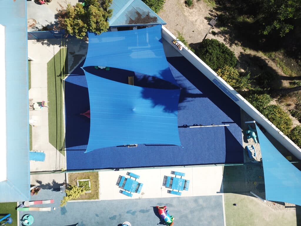Aerial view of shade sails over a blue poured-in-place rubber play area