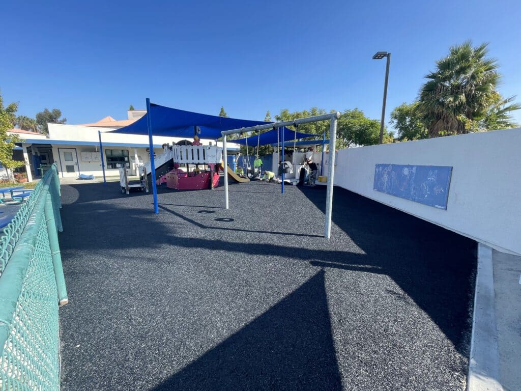 Gray poured-in-place rubber play area under blue shade sails
