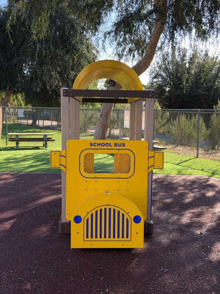 Yellow bus-themed play structure on terra cotta poured-in-place rubber in a park