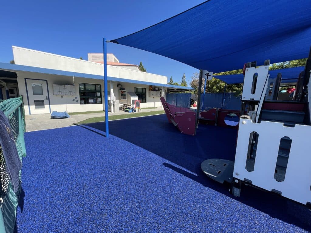 Blue poured-in-place rubber under shade sails beside a building