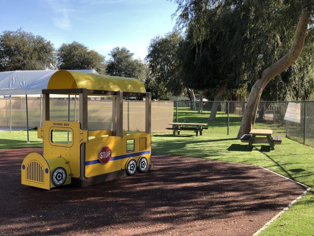 Yellow bus play structure on terra cotta poured-in-place rubber beside a park lawn