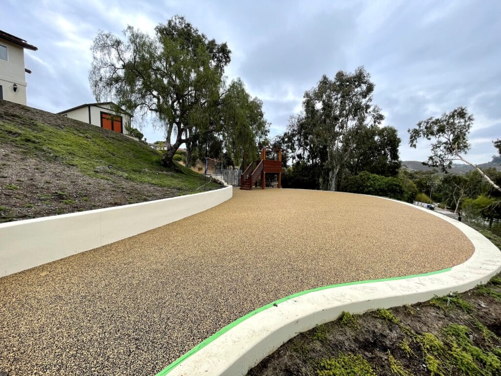 Tan porous rubber pathway along a hillside with a concrete curb