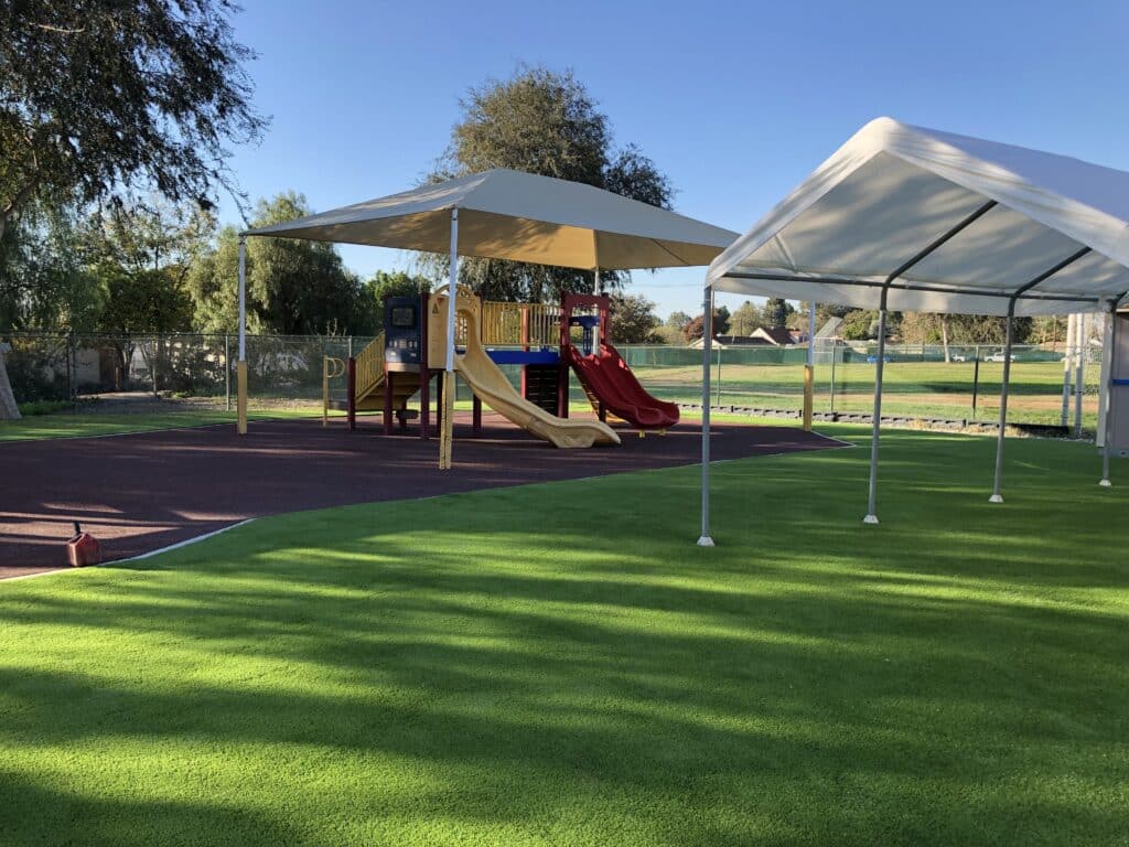 Shade structures over a synthetic turf playground with play equipment