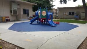 Octagonal blue poured-in-place rubber play area around a play structure beside a school building