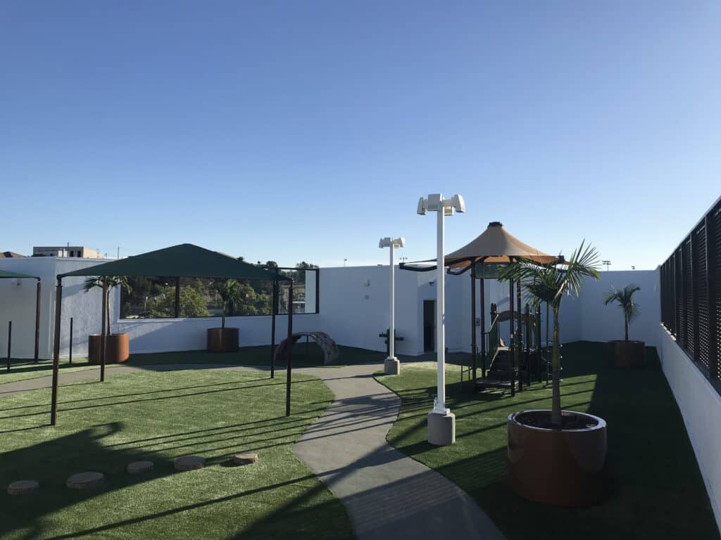 Shade structures over a turf play area beside a building