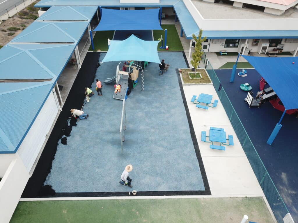 Light-blue rubber surface with a shade sail at a building